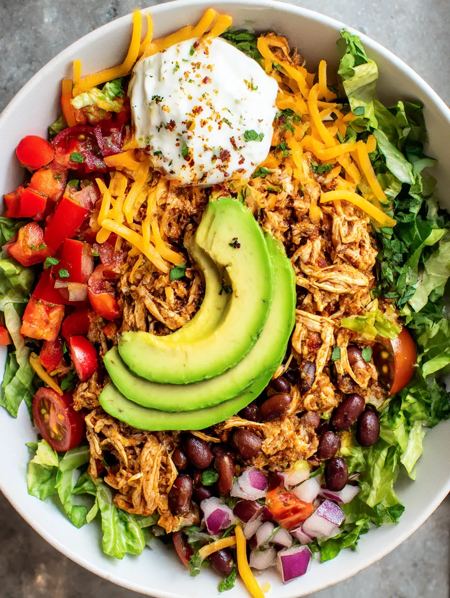 A bowl filled with shredded chicken salad, colorful toppings, and crispy lettuce.