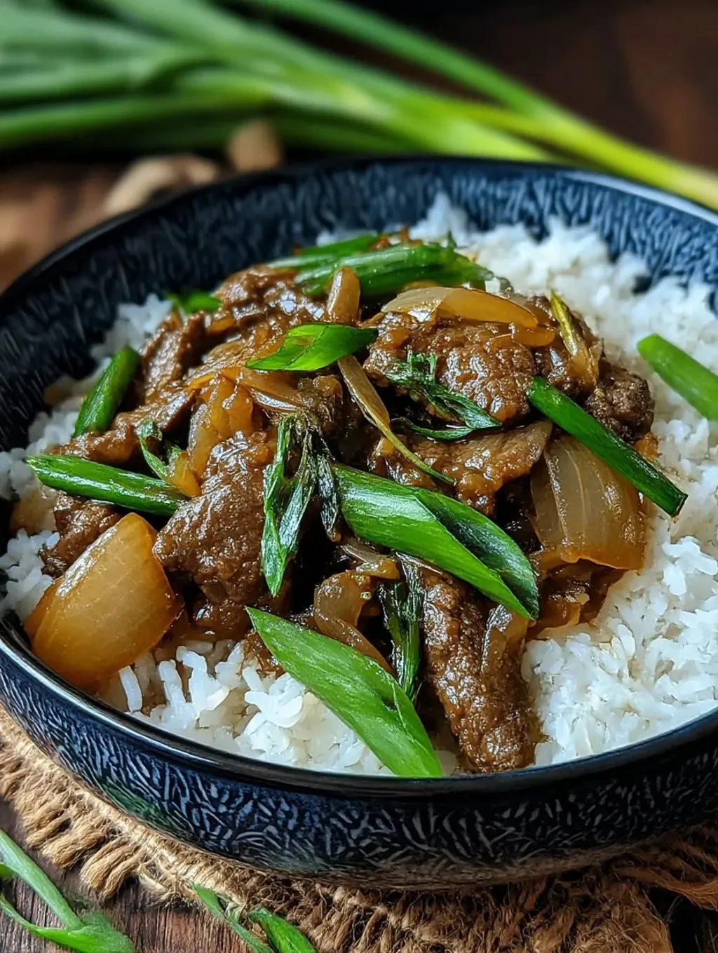 A sleek black bowl filled with Chinese-style beef and onions stir fry.