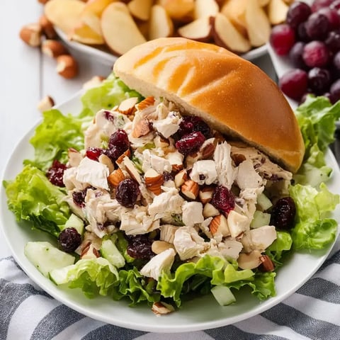 Greens holding chicken salad with nuts and cranberries. Sandwich bun and apple slices on the side.