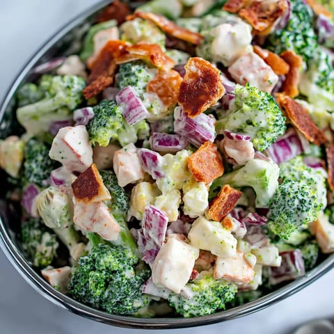 A close-up bowl of bacon, broccoli, cauliflower, and red onion in a creamy dressing.