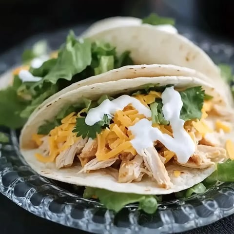 Three flavorful tacos stuffed with shredded chicken, cheese, lettuce, and sour cream on a pretty plate.