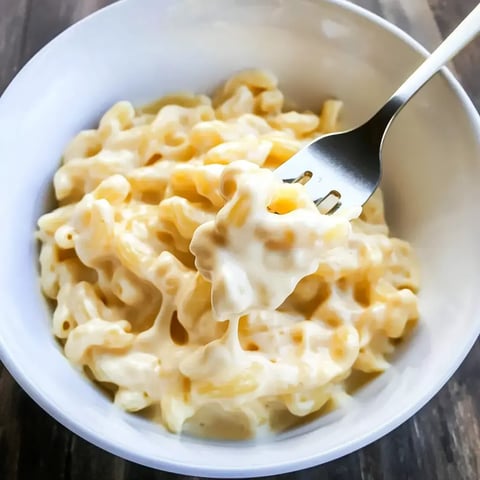 Fork lifting cheesy macaroni from a bowl of creamy pasta.