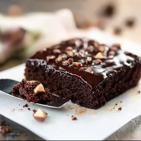 A glossy chocolate cake with nuts and a slice on a plate next to a serving utensil.