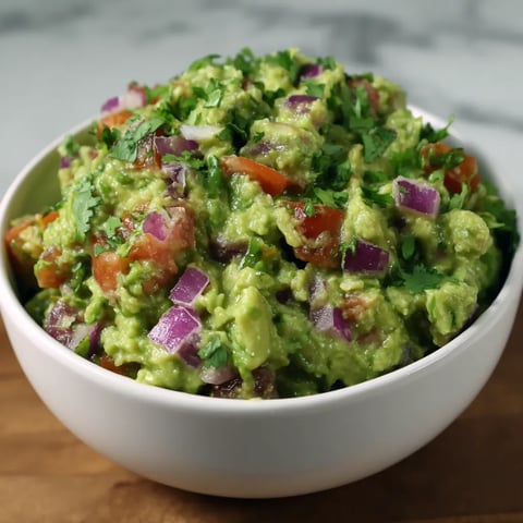 A bowl of guacamole with tomatoes and onions.