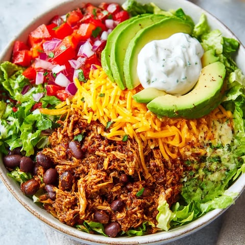 A big bowl with lettuce, tomato pieces, avocado slices, and a dollop of sour cream.
