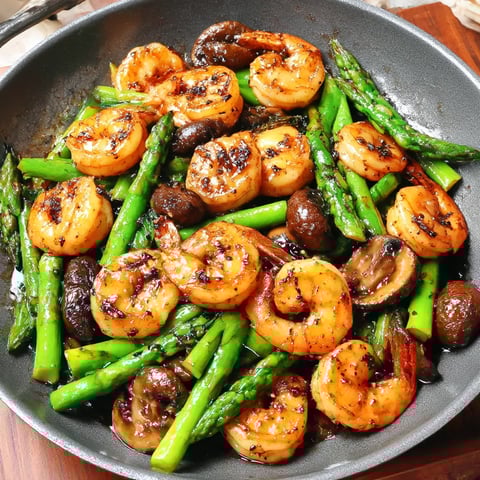 Shrimp, asparagus, and mushrooms sizzle together in a hot pan.