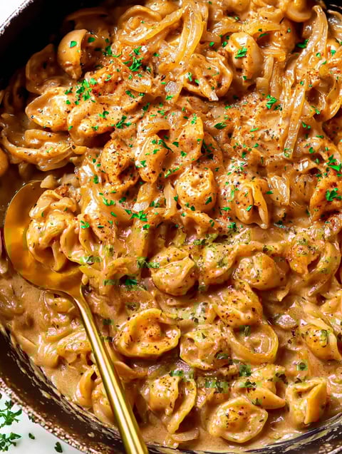 Eine Schüssel mit Pasta, die mit Parmesan und Zwiebeln garniert ist.