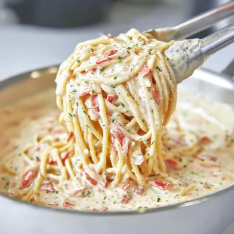A spoon dips into a bowl packed with pasta.