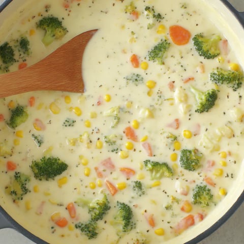 Chunky vegetable chowder with cheese, scooped by a wooden spoon.
