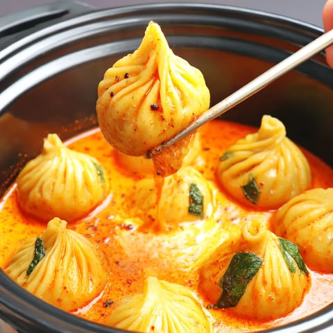 There's a spoon resting in a steaming bowl filled with plump dumplings.