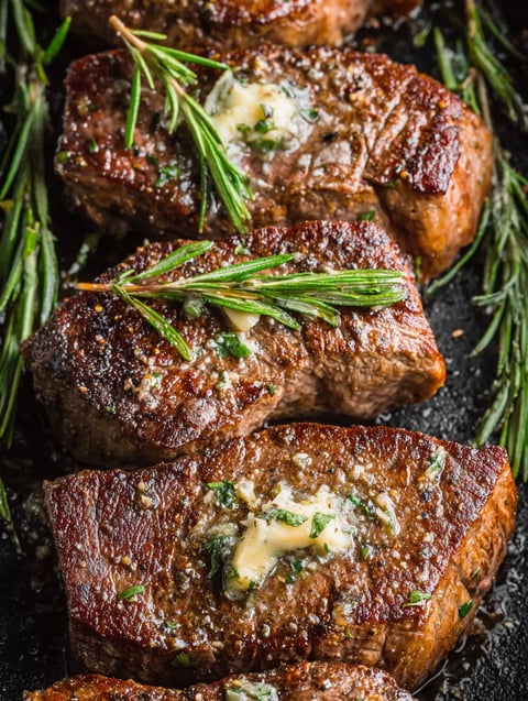 Two beef steaks with butter and herbs on a plate.