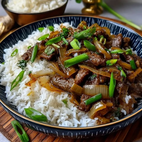 A plate piled with Chinese beef and onions stir fried and served with rice.