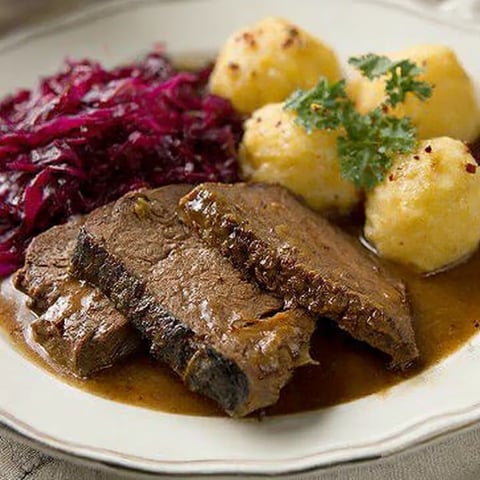A plate piled with grilled beef, potatoes, sauerkraut, and melted cheese.